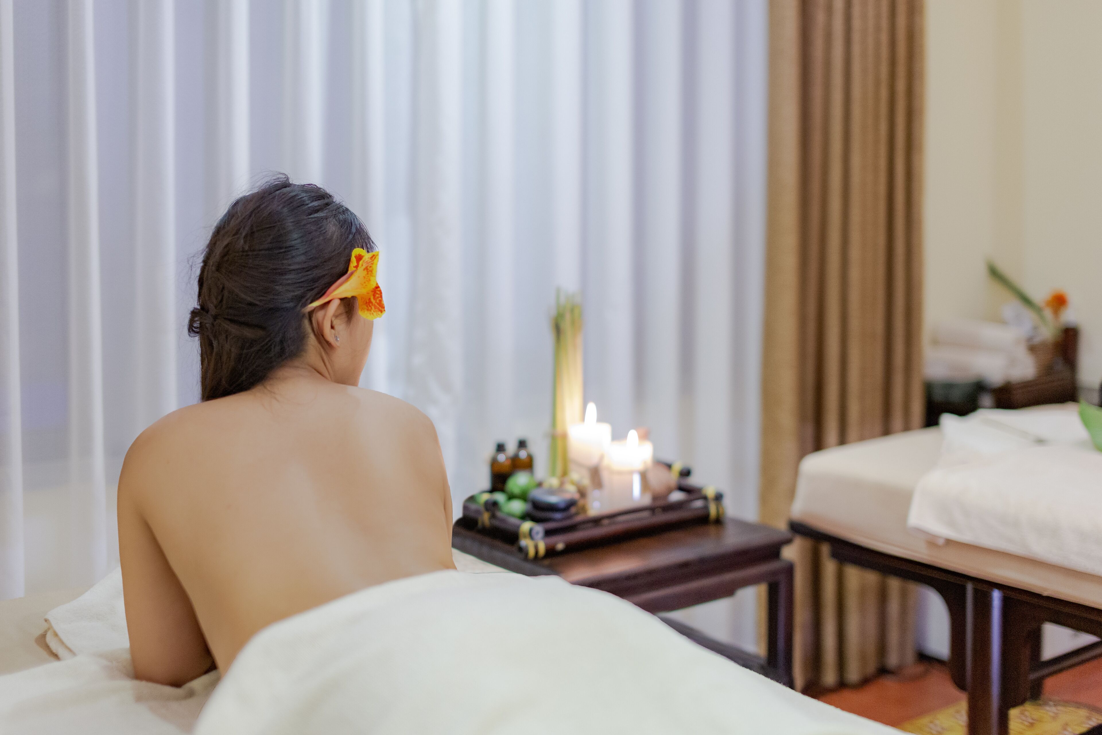 A spa room with a bed, a small table with candles, and a window with curtains.