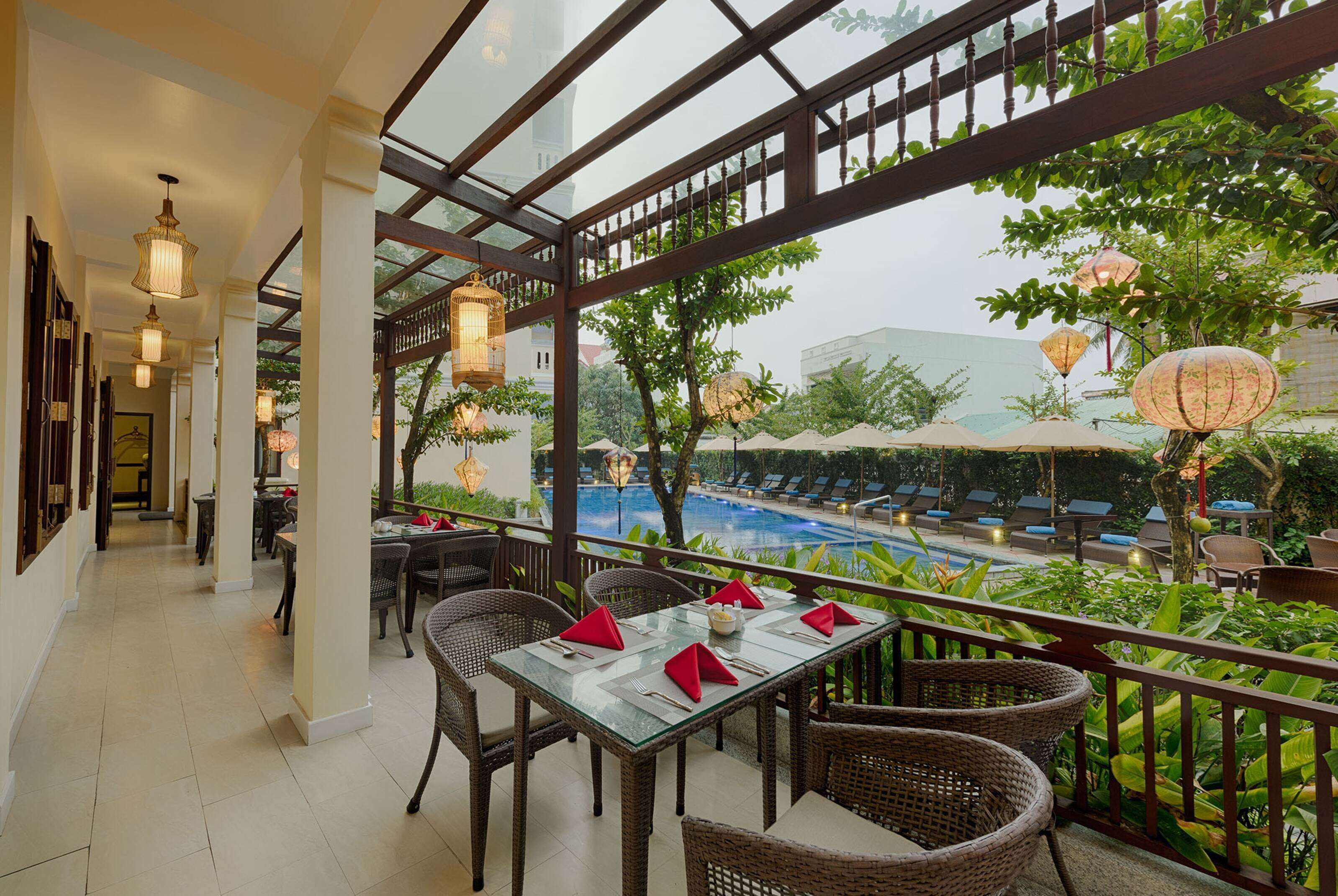 A restaurant with a glass table and wicker chairs, overlooking a pool and lush greenery.