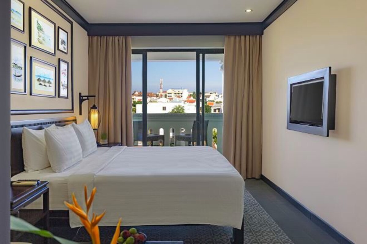 Quarto de hotel com cama, televisão, janela com cortinas e quadros na parede.