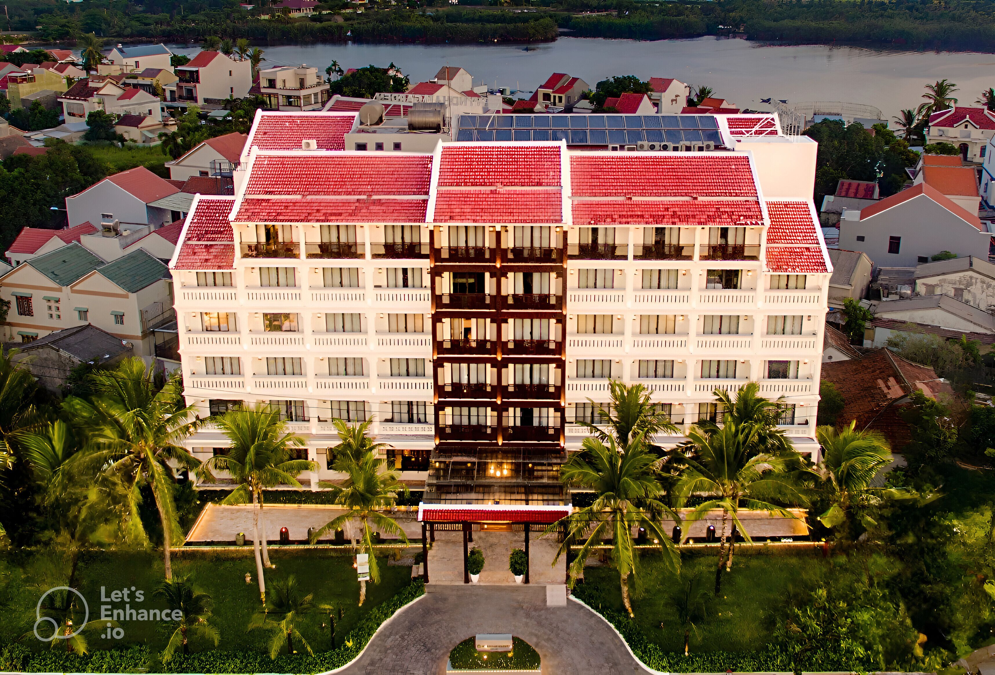A large hotel with a red roof and multiple floors, surrounded by palm trees and other buildings.