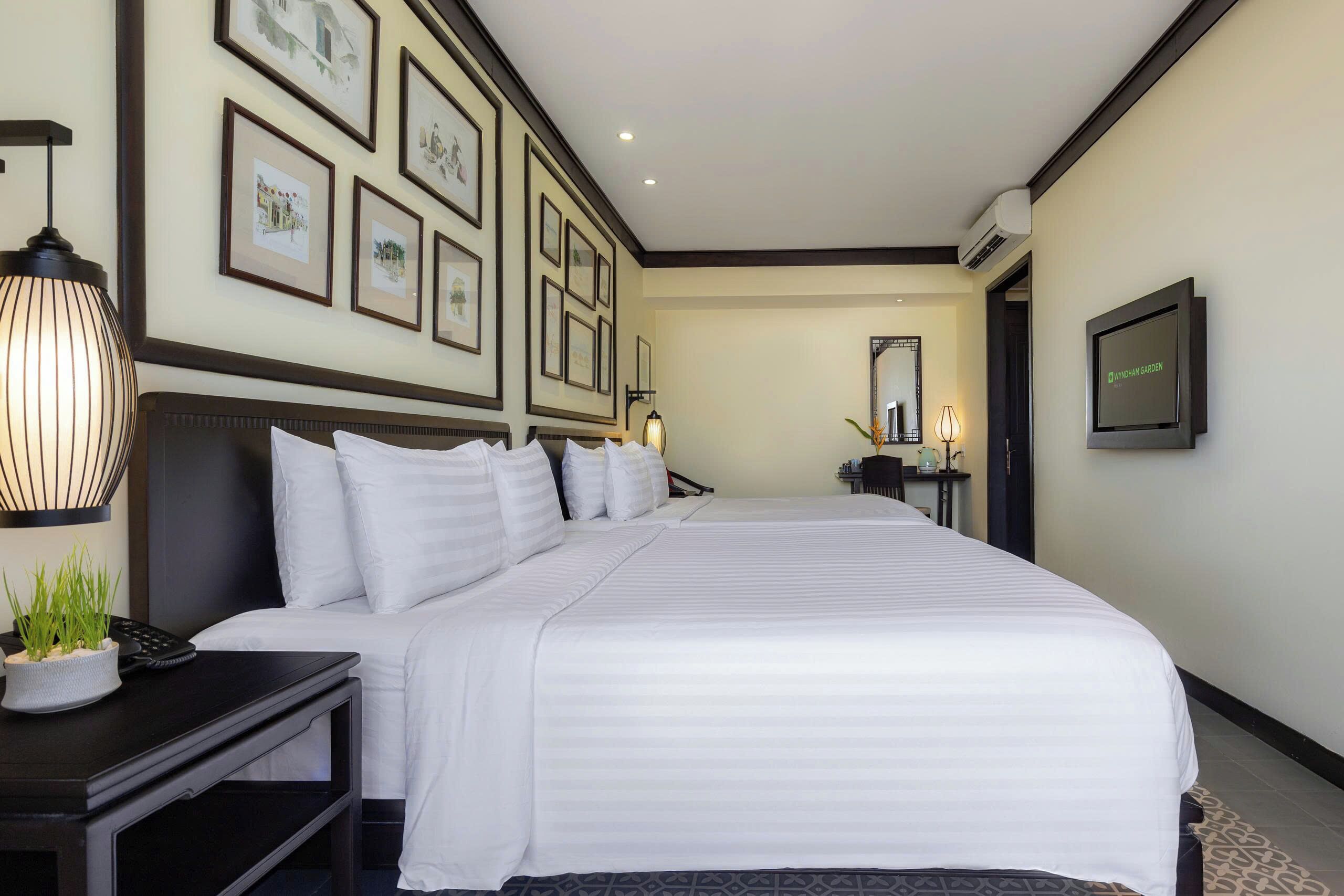 A hotel room with a large bed, a bedside table with a lamp, a TV, and framed pictures on the wall.