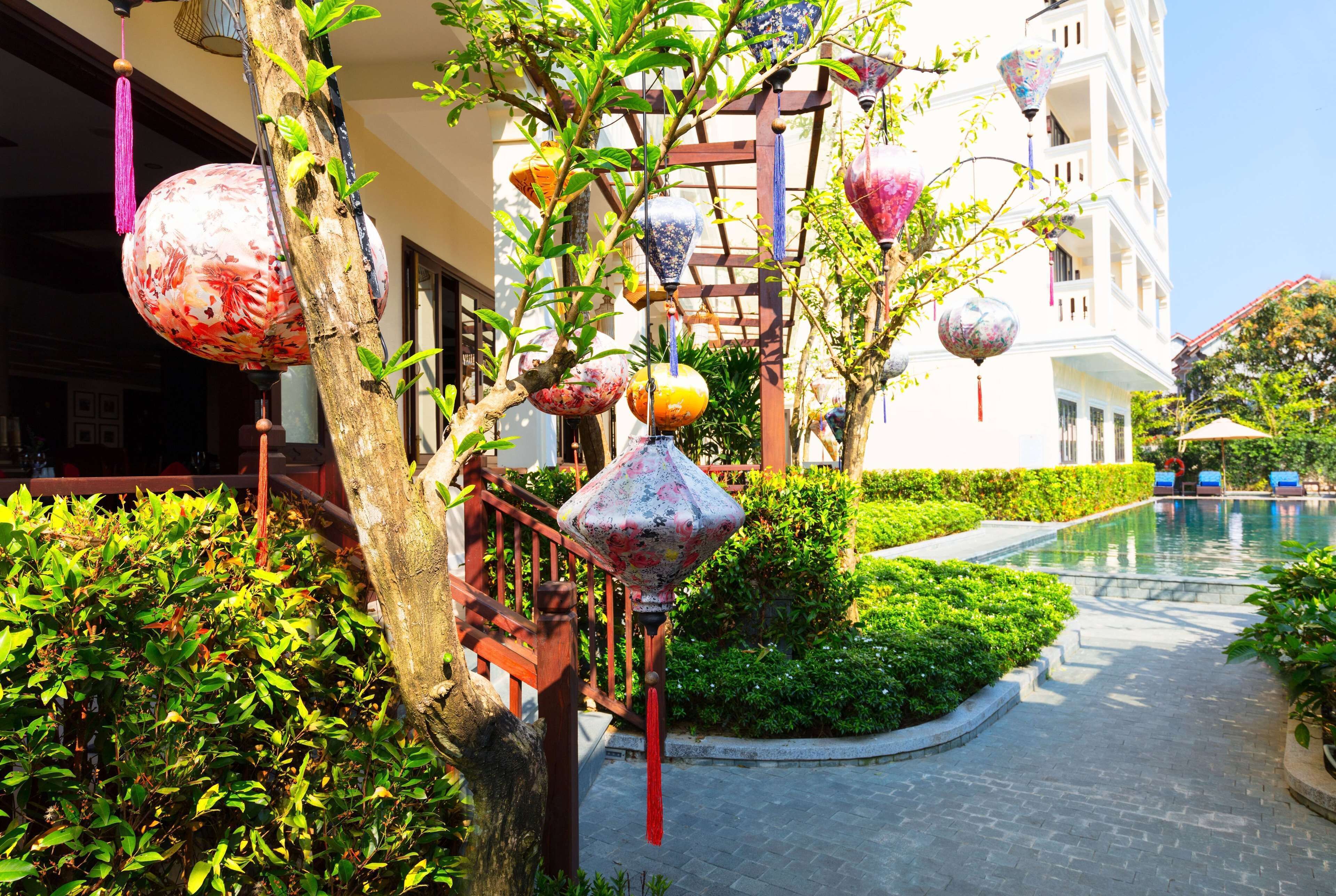 A hotel with a pool, lush greenery, and decorative lanterns.