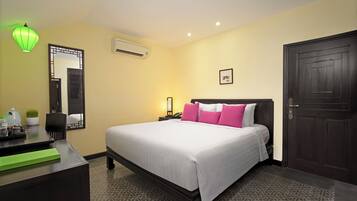 A hotel room with a bed, bedside table, lamp, air conditioning unit, and a door.