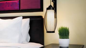 A neatly made bed with white linens, a black nightstand with a white pot of green plants, and a modern wall-mounted light fixture.