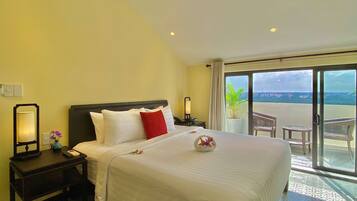 A hotel room with a large bed, a nightstand with a lamp, a vase with flowers, and a view of the outside balcony.