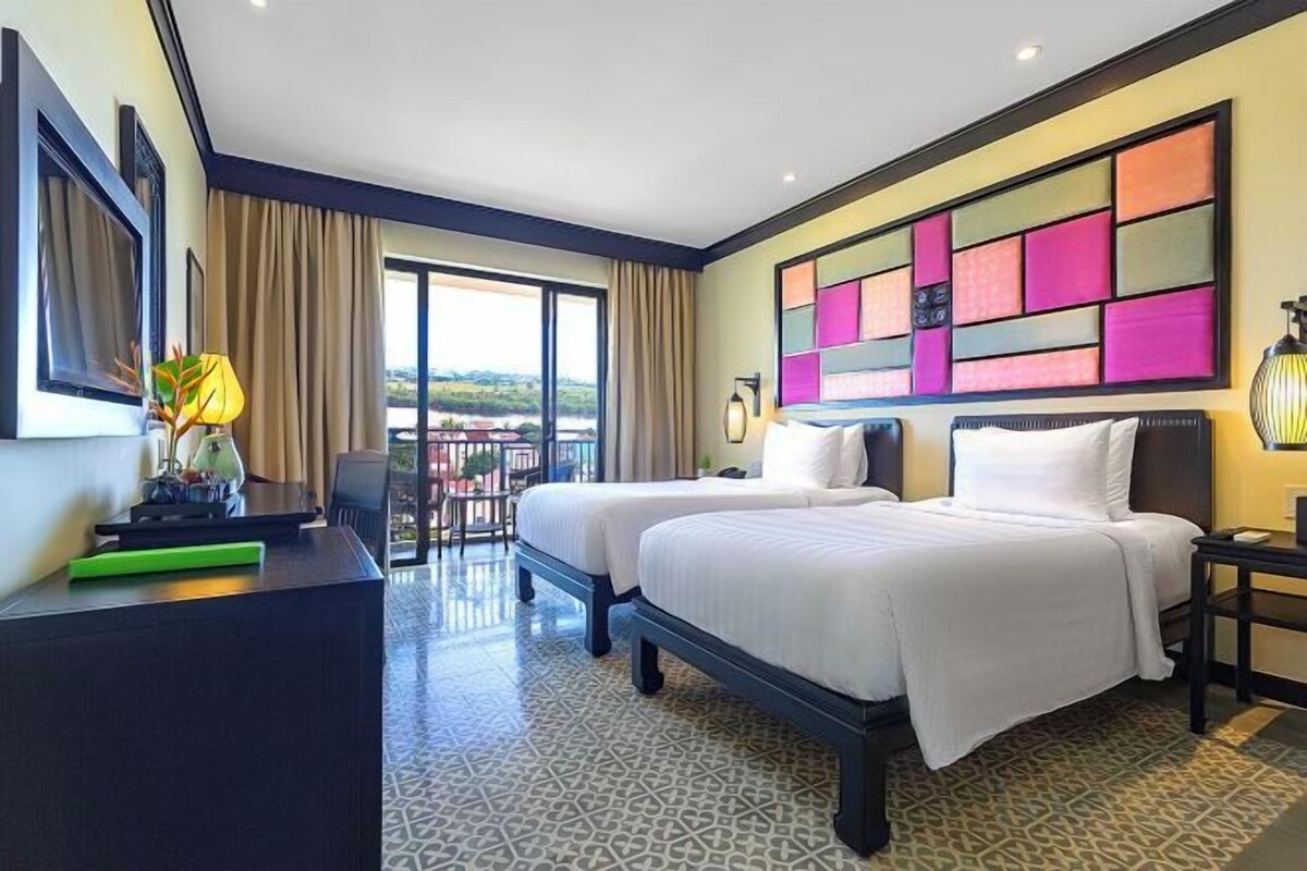 Habitación de hotel con dos camas, un escritorio, una silla, un balcón y un ventanal grande.