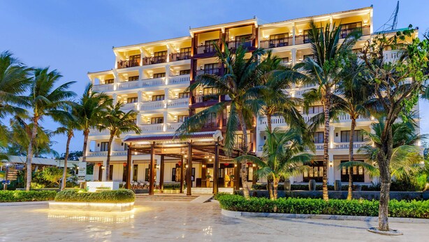 Un hotel de varios pisos con balcones, palmeras y una entrada bien iluminada.