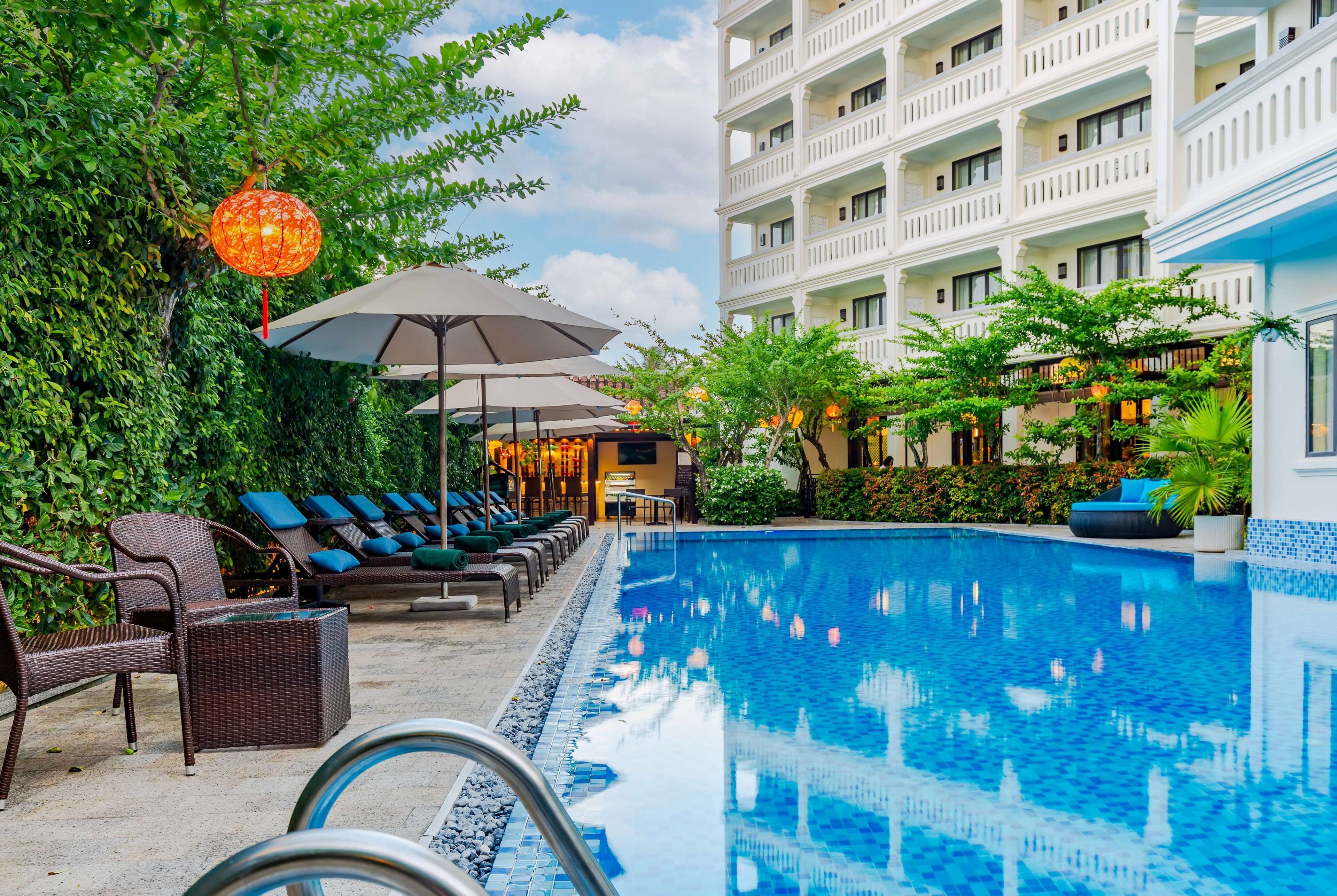 A pool area with lounge chairs, umbrellas, and a building with balconies.