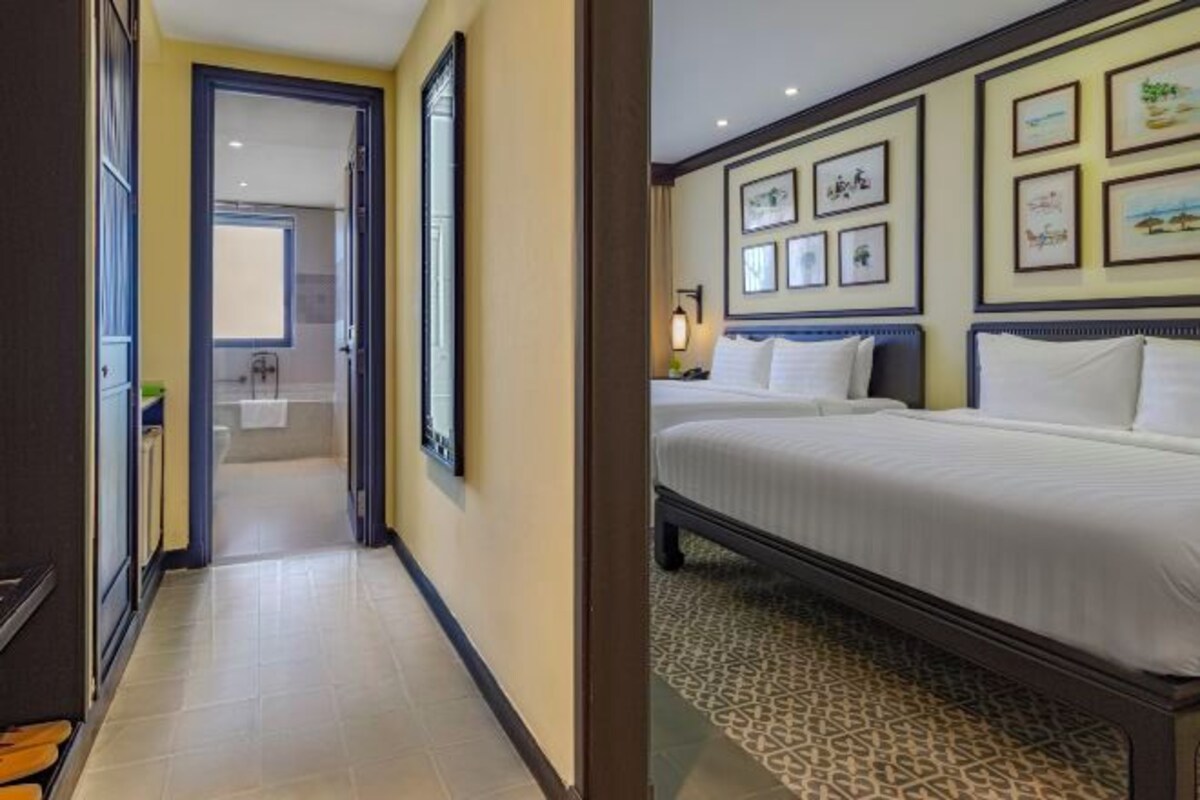 A hotel room with a bed, a bathroom with a shower, and a hallway leading to another room.
