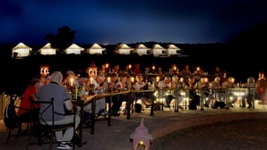 A group of people dining at an outdoor restaurant with tents in the background. - Raisar Camp (Bikaner)