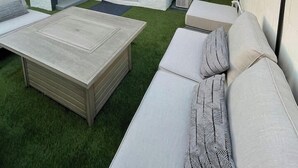 Ein moderner Außenbereich mit Holztisch, einer Sitzecke und einer Treppe zu einem Balkon.