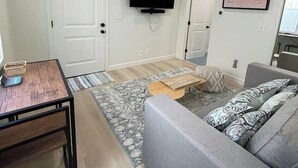 Ein modernes Wohnzimmer mit einer Couch, einem Couchtisch, einem an der Wand montierten Fernseher und einer Tür zu einem anderen Raum.