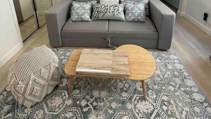 Ein modernes Wohnzimmer mit einem grauen Sofa, gemusterten Kissen, einem Holztisch und einem Teppich mit Muster.