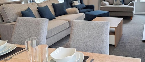 Un salon moderne avec un coin repas, comprenant un ensemble de canapés, une table basse et une table à manger avec des assiettes et des verres.
