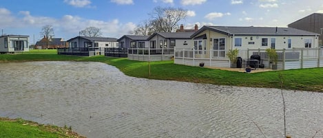 A residential area with houses along a water body, featuring a grassy lawn and a paved walkway.