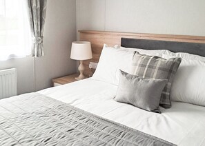 A neatly made bed with a quilted blanket, a bedside lamp, and two pillows.