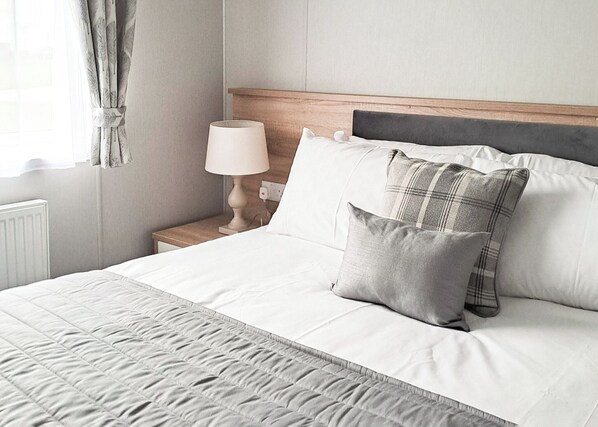 Una cama bien hecha con un edredón acolchado, una lámpara de noche y dos almohadas.