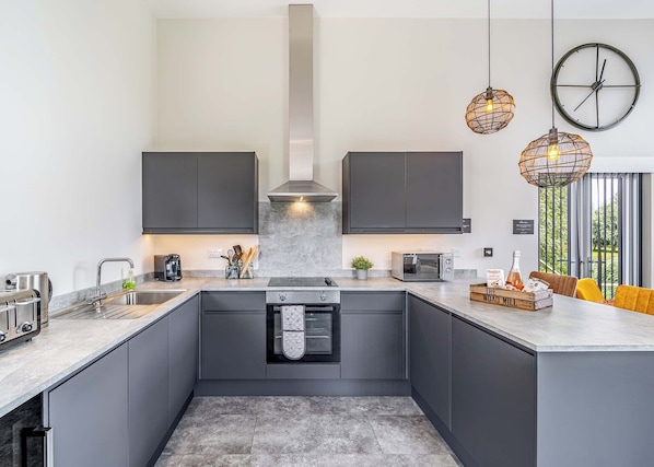 A modern kitchen with dark cabinetry, a central island, a built-in oven, and pendant lighting.