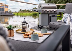 A cozy outdoor seating area with a grill, a coffee pot, and a tray with bread and cookies. - Muntjac Lakeside Lodge (Boston)
