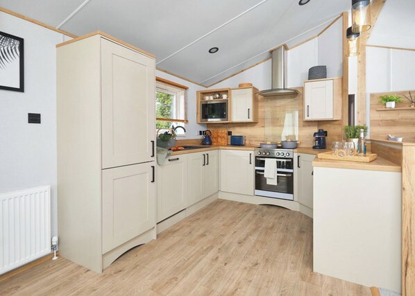 A compact kitchen with white cabinets, a stove, and a microwave. - Lodge Hot Tub 4 Bed No Pets (Clarach Bay, Nr Aberystwyth)