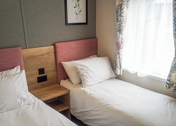 Een éénpersoonskamer met twee bedden, een houten hoofdbord, een nachtkastje en een raam met gordijnen.