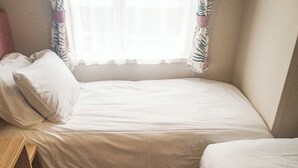 A small, single-bed room with a window, a bedside table, and a chair.