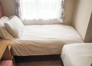 Ein kleines Zimmer mit einem Einzelbett, einem Fenster, einem Nachttisch und einem Stuhl.