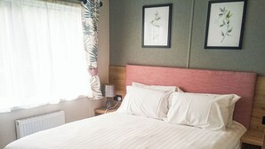 A neatly made bed with white linens, a wooden nightstand with a lamp, and two framed botanical prints on the wall.
