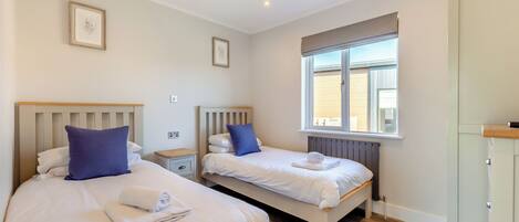 A hotel room with two beds, a window with a view, a radiator, and a wooden floor.