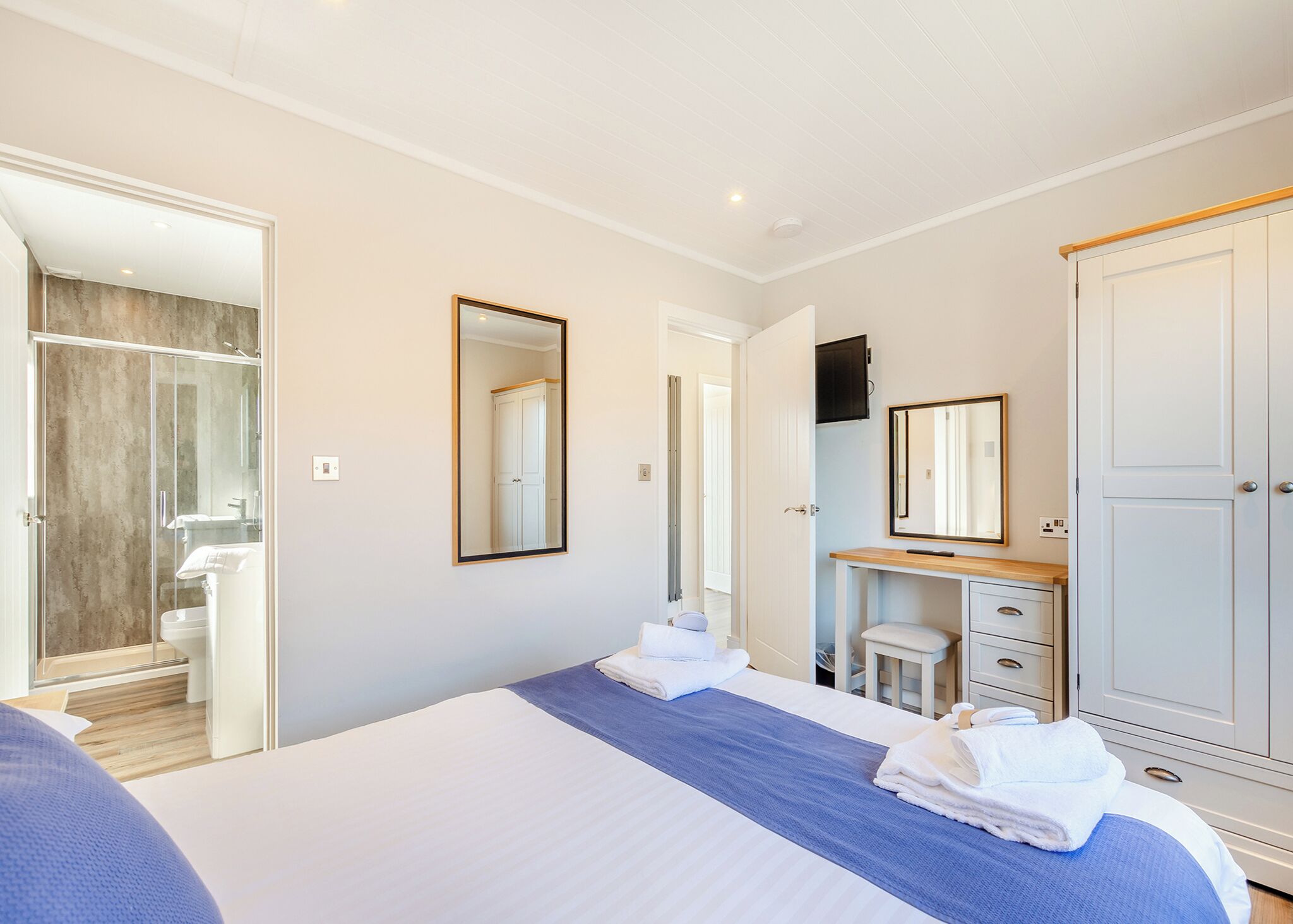 Une chambre d’hôtel avec un lit, un miroir, une armoire et une salle de bain visible à travers une porte ouverte.