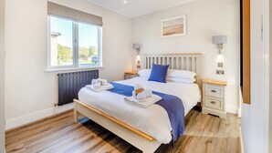 A modern hotel room with a large bed, bedside tables, a window, and a view of the outside.