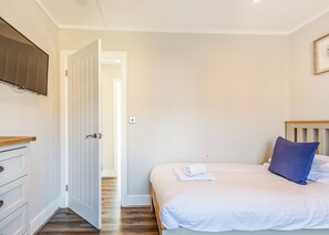 A bedroom with a bed, a TV mounted on the wall, a wooden dresser, and a door leading to another room.