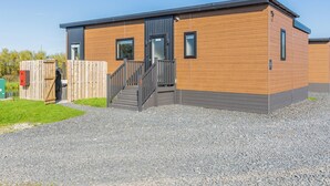 A modern building with a wooden exterior, a staircase leading to the entrance, and a small outdoor area with a wooden fence.