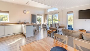 A modern kitchen with a central island, a dining area with a wooden table, and a living room with a sofa and TV.