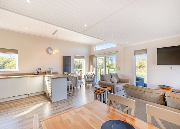 A modern kitchen with a central island, a dining area with a wooden table, and a living room with a sofa and TV.