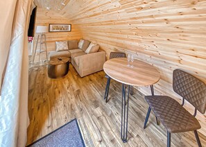 A cozy interior with a wooden ceiling, a sofa, a round table with chairs, and a sign on the wall.