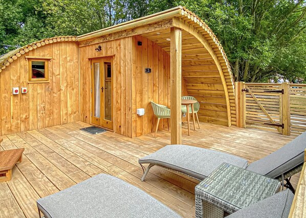 A wooden cabin with a covered patio, two chairs, and a table.