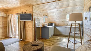 Um alojamento pequeno com cozinha compacta, televisão de ecrã plano na parede e zona de refeições com mesa de madeira.