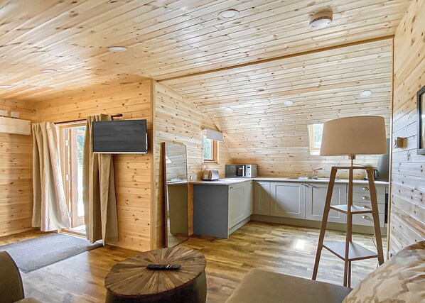 Una cabaña compacta con kitchenette, un televisor de pantalla plana en la pared y un comedor con mesa de madera.