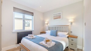 A bedroom with a bed, bedside tables, a window, and a wall-mounted light fixture. - 3 bedroom accommodation in Poulton-Le-Fylde (Poulton-Le-Fylde)