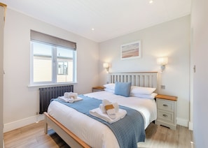 A bedroom with a bed, bedside tables, a window, and a wall-mounted light fixture.