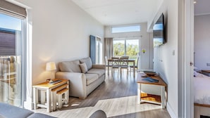 A modern living room with a sofa, dining table, and chairs, a TV mounted on the wall, and a large sliding glass door leading to a balcony. - 3 bedroom accommodation in Poulton-Le-Fylde (Poulton-Le-Fylde)