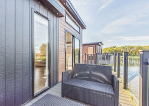 A modern building with large sliding glass doors, a wicker chair, and a wooden deck overlooking a body of water.