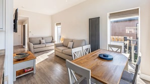 A modern living room with a sofa, dining table, and chairs. There is a window with curtains, a door, and a view of the outside. - 3 bedroom accommodation in Poulton-Le-Fylde (Poulton-Le-Fylde)