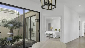 A modern hotel room with a glass door leading to a patio, a round table in the foreground, and a bed with a white bedspread and pillows in the background. - Premium PGA West Location Large Saltwater Pool/Spa Fire Pit Spectacular Mtn Views: #067312 (La Quinta)