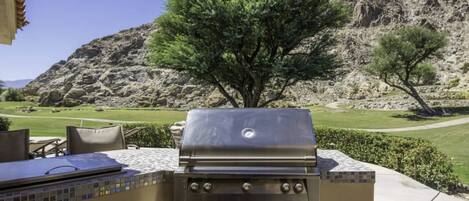 An outdoor grill with a tiled backsplash and a view of a golf course and mountains in the background.
