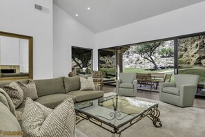 Relax in this stylish living room with a sofa, armchair, and glass coffee table, offering a view of the landscaped outdoor area and rocky landscape.