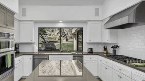 A modern kitchen with white cabinetry, a large window overlooking a backyard, and a built-in dishwasher. - Premium PGA West Location Large Saltwater Pool/Spa Fire Pit Spectacular Mtn Views: #067312 (La Quinta)