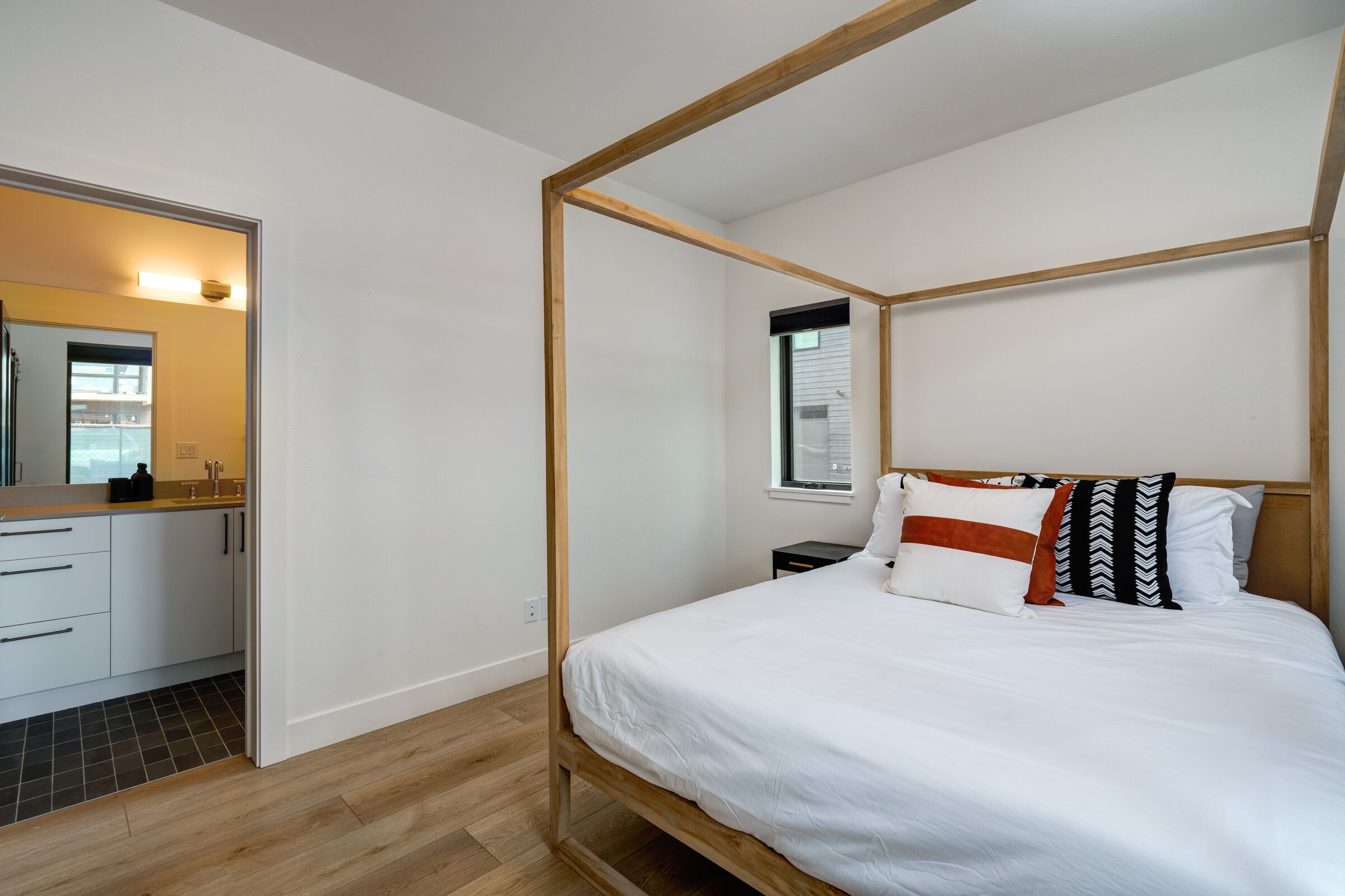 Un dormitorio moderno con una cama con dosel, una mesita de noche pequeña y un ventanal con persianas.