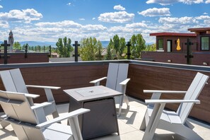 A rooftop patio with white chairs and a table, overlooking a residential area with houses and a mountain range. - Rooftop Retreat! Pet friendly, Gorgeous Rooftop Sanctuary with Hot Tub and Firepit (Steamboat Springs)